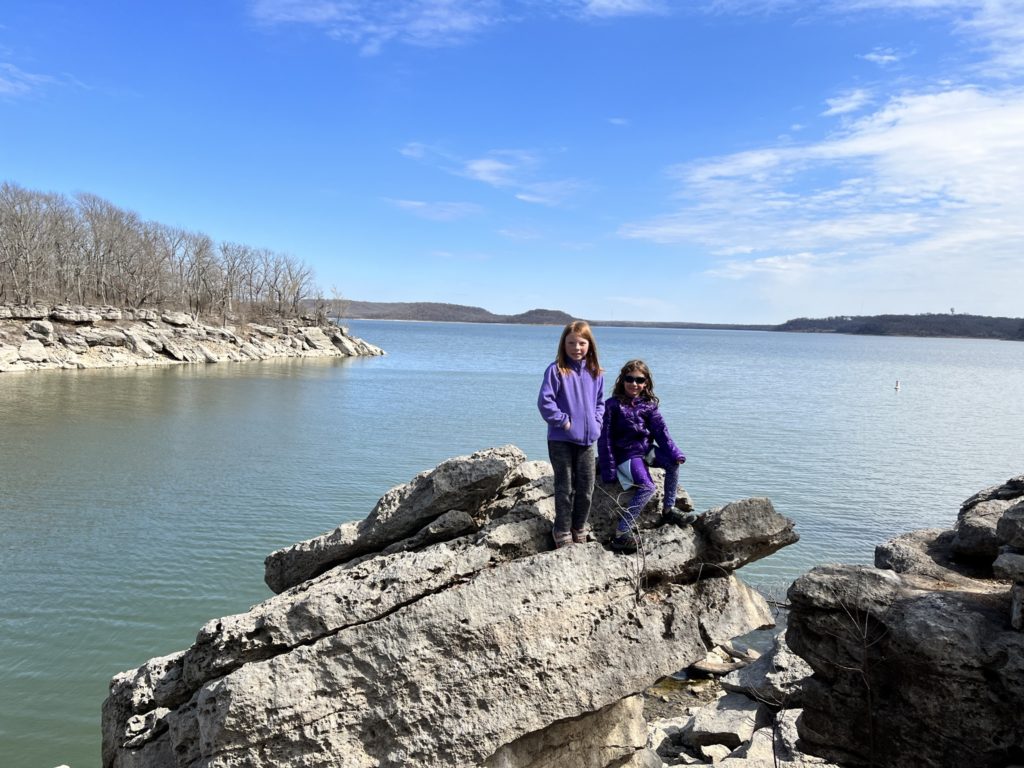 A photo of Nora and Ainsley sitting on a large rock overlooking a lake