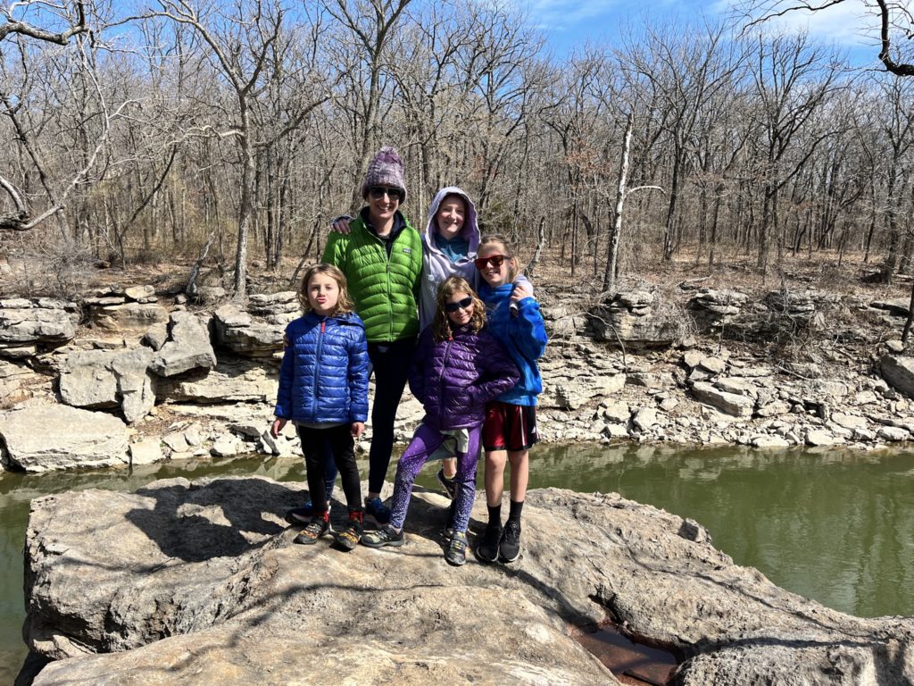 A photo of Grayson, Kelsey, Rayleigh, Ainsley, and Dillon wearing coats posing on a large rock in front of a body of water