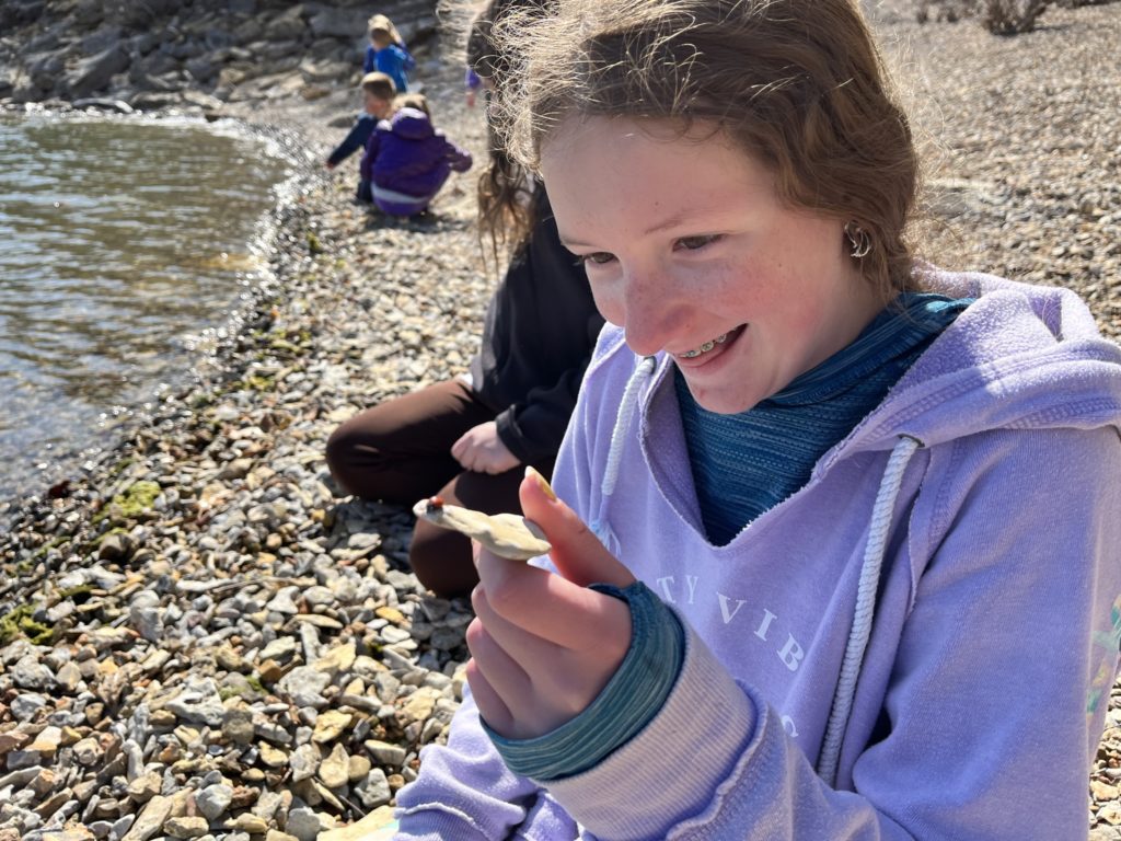 A photo of Rayleigh excitedly looking at a ladybug on a rock she found at a rocky beach next to a lake