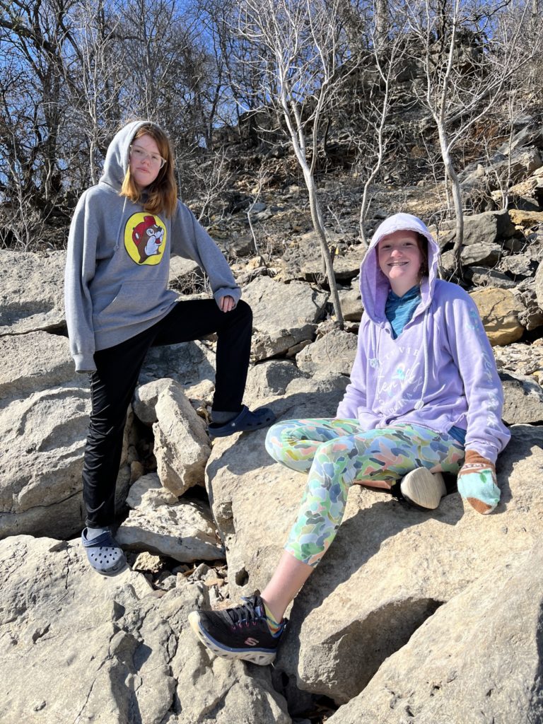Kate and Rayleigh both wearing hoodies with the hoods up posing on some rocks with trees in the background