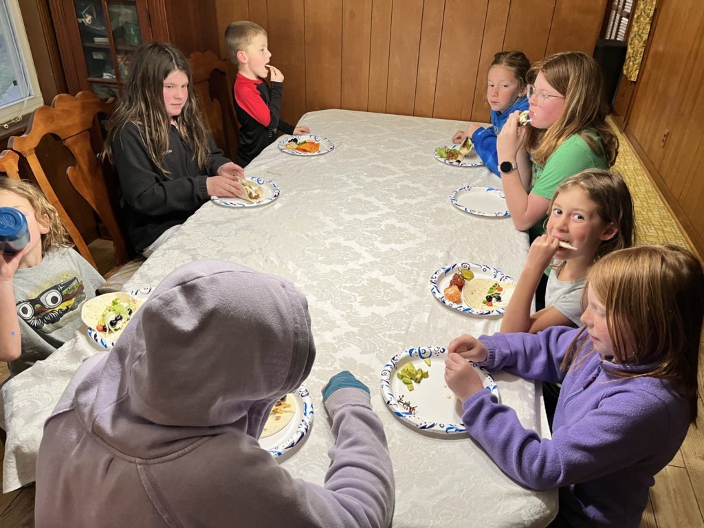 A photo of Grayson, Molly, Oliver, Dillon, Kate, Ainsley, Nora, and Rayleigh sitting at a table eating tacos