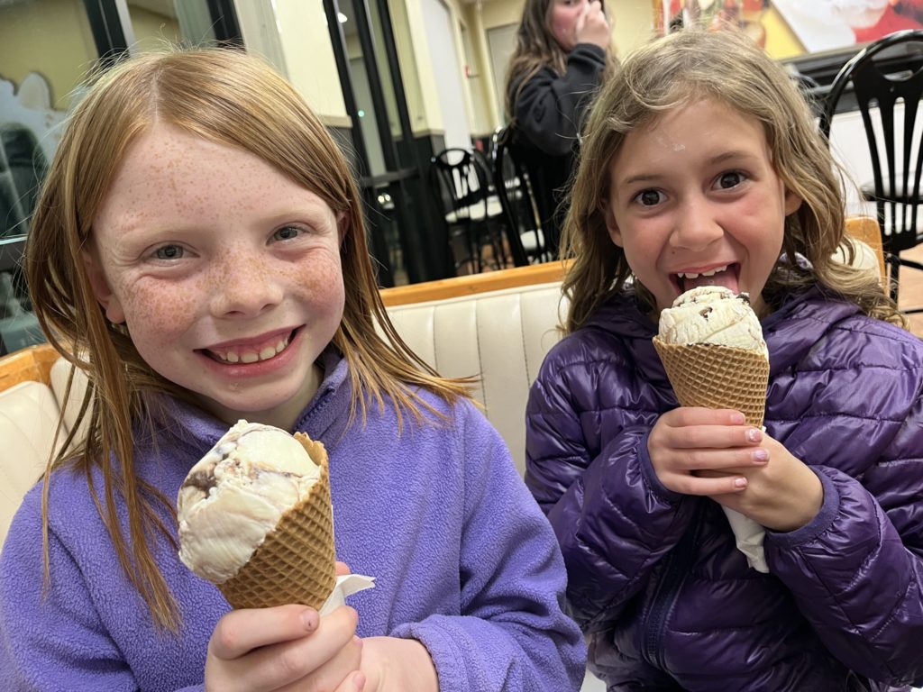A photo of Nora and Ainsley, both dressed in purple, eating ice cream cones in a restaurant