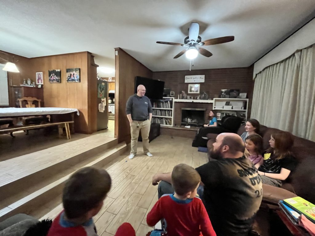 A photo of Kevin standing in a living room with Kirk, the Wendell kids, and the Forrester kids sitting on couches listening to him