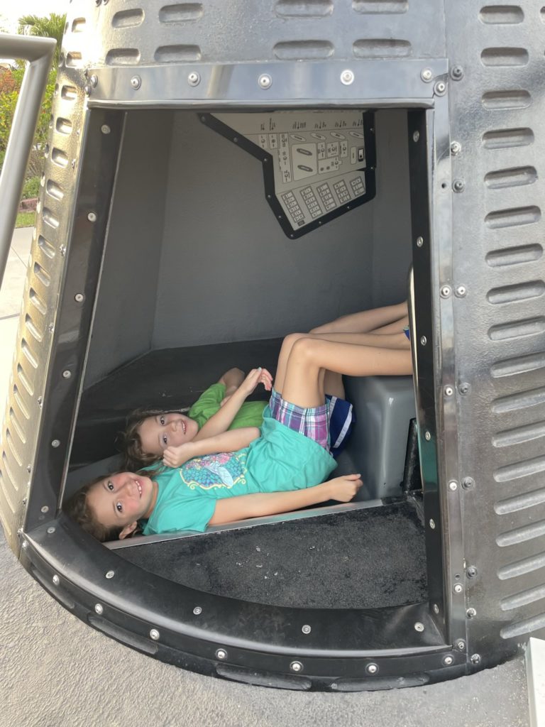 A photo of Ainsley and Grayson laying down in seats in a replica of a space capsule