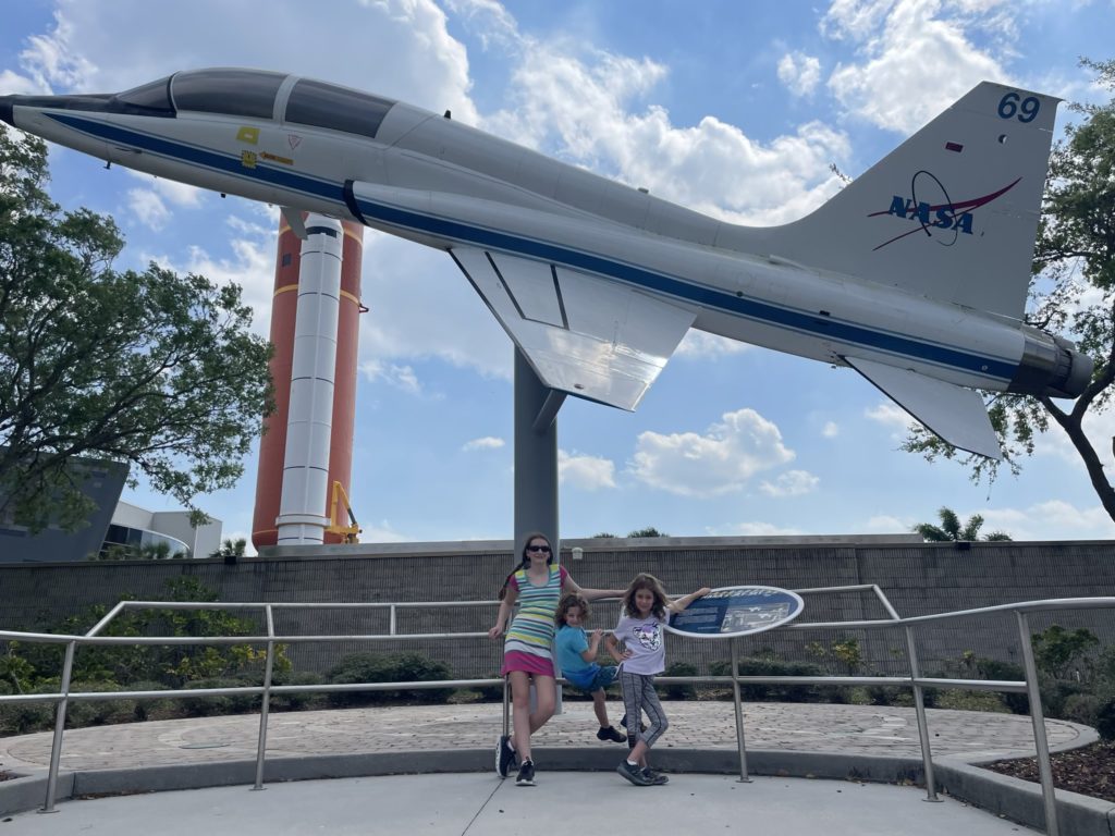 A photo of Rayleigh, Grayson, and Ainsley in front of a space shuttle training jet