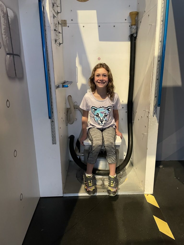 A photo of Ainsley sitting on a replica of a space station toilet