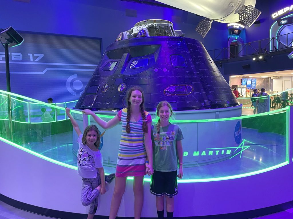 A photo of Ainsley, Rayleigh, and Dillon standing in front of a space capsule