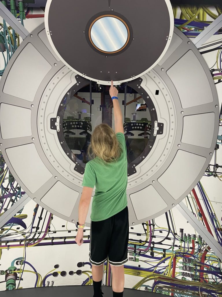 A photo of Dillon touching part of a replica of the inside of a space capsule