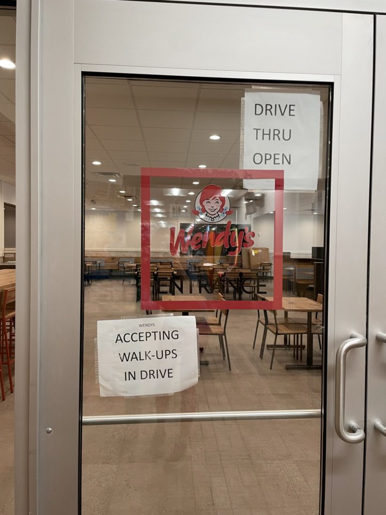 A photo of the door to a Wendy's, with signs that read "drive thru open" and "accepting walk-ups in drive"
