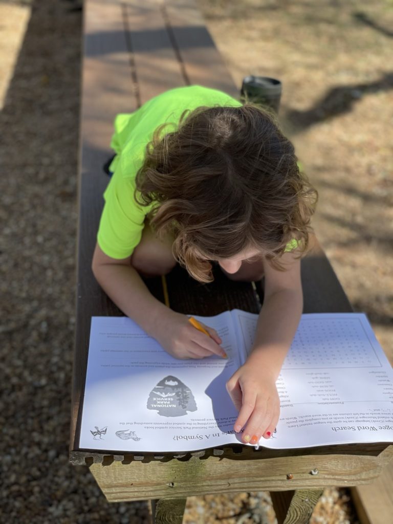 A photo of Grayson filling out his Junior Ranger book on a bench outside