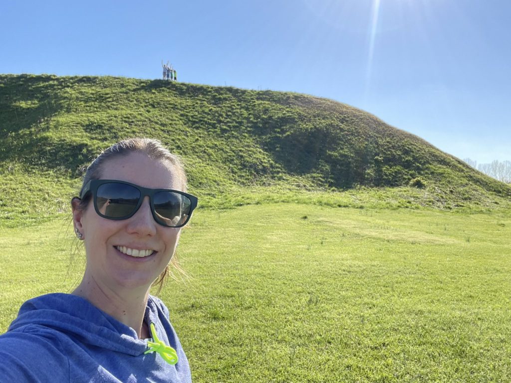 A photo of Kelsey in the foreground with Rayleigh, Dillon, Ainsley, and Grayson standing atop Great Temple Mound far in the background