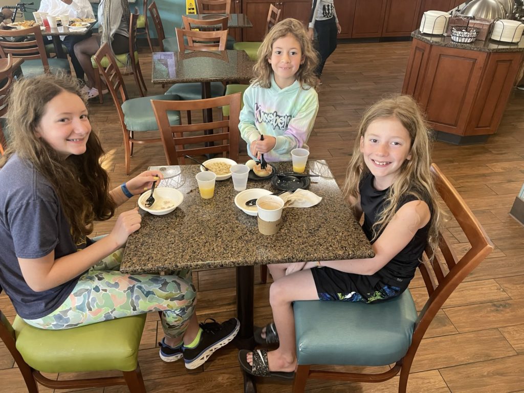 A photo of Rayleigh, Ainsley, and Dillon eating breakfast at a table in a hotel's common area