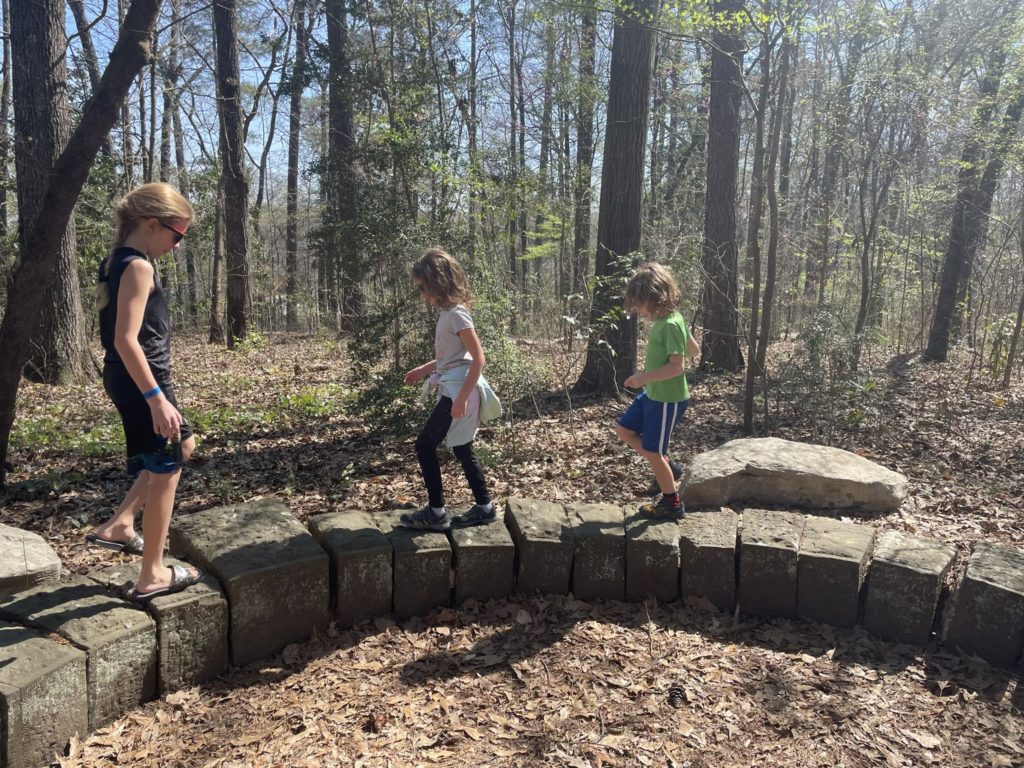 A photo of Dillon, Ainsley, and Grayson walking along a low rock wall
