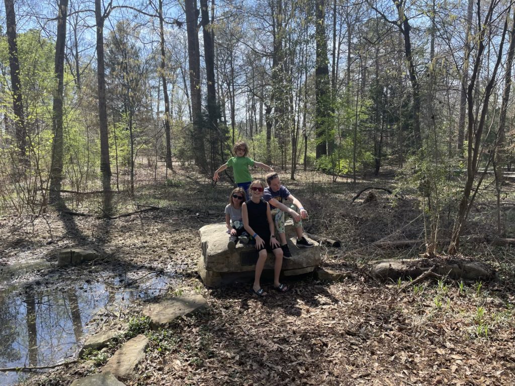 A photo of Ainsley, Grayson, Dillon, and Rayleigh sitting on a rock by a pond