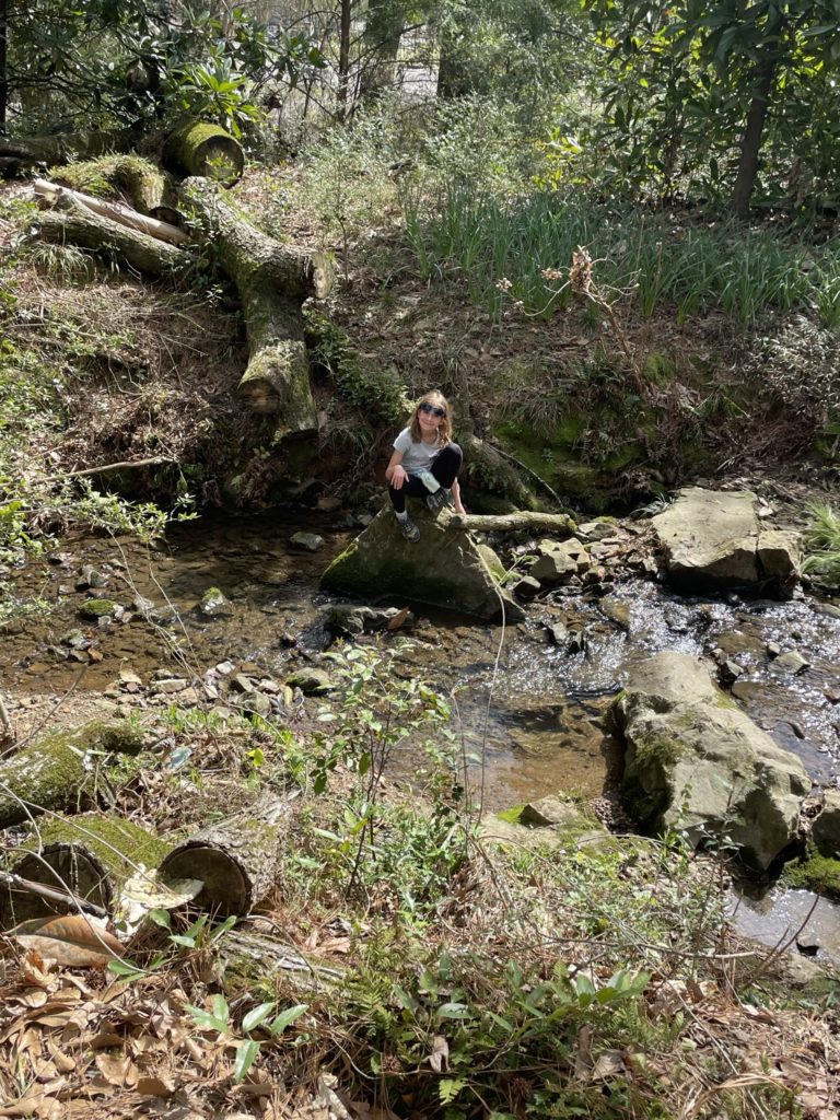 A photo of Ainsley sitting on a rock overlooking a stream