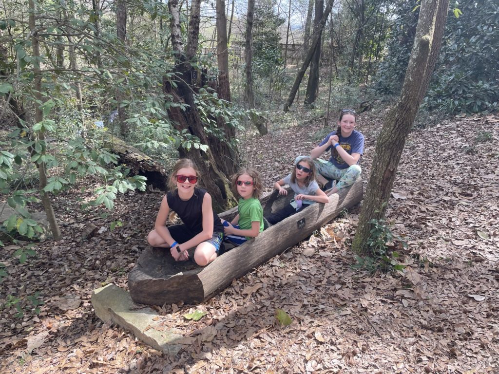 A photo of Dillon, Grayson, Ainsley, and Rayleigh sitting in a dugout canoe in the woods