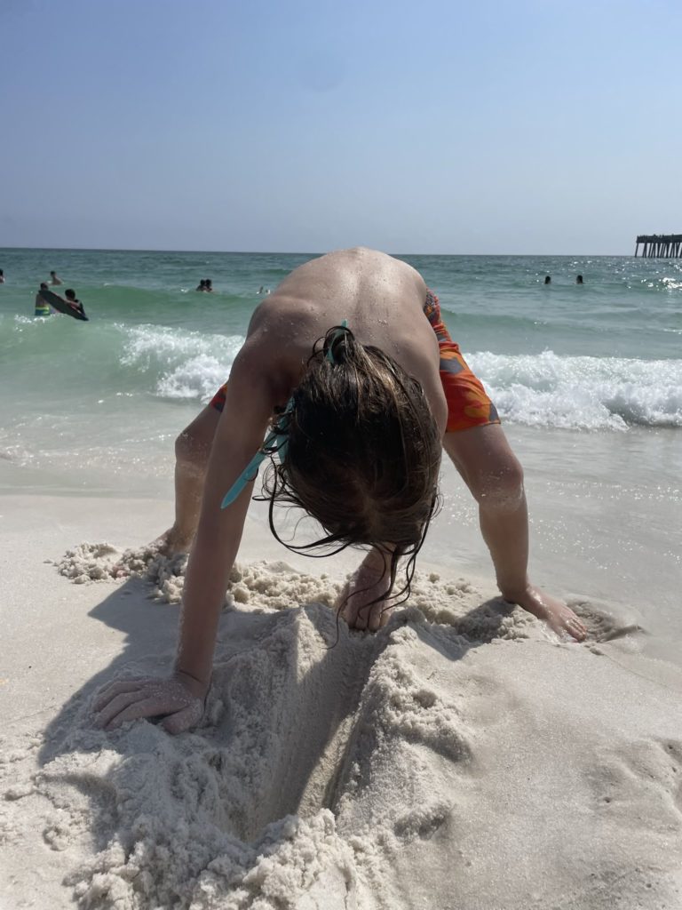 A photo of Grayson digging in the sand next to the water's edge