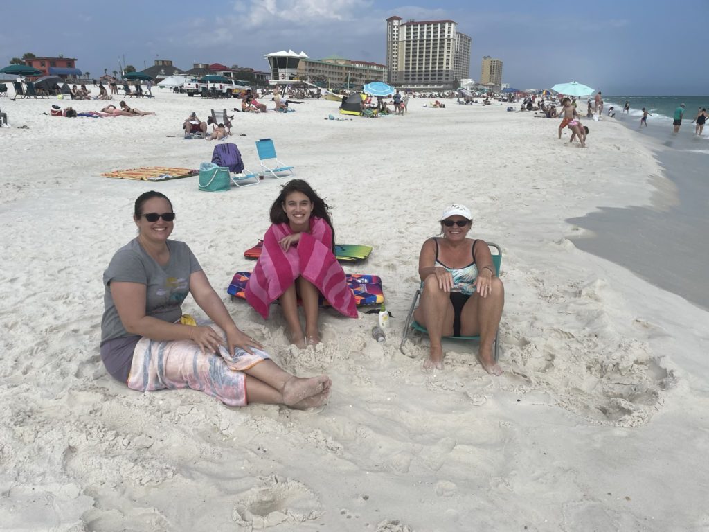 A photo of Kim, Kahlan, and Karen sitting on the beach