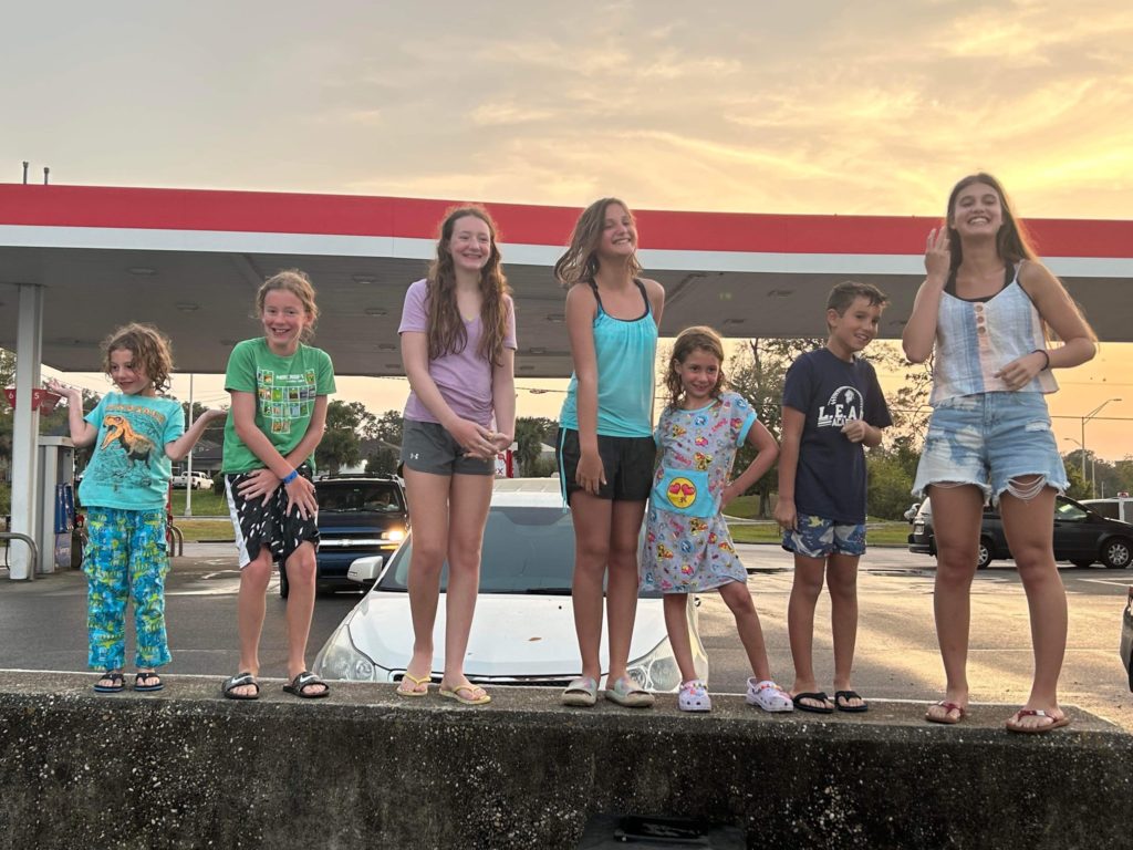 A photo of Grayson, Dillon, Rayleigh, Niala, Ainsley, Riker, and Kahlan standing on top of a concrete barrier near a gas station