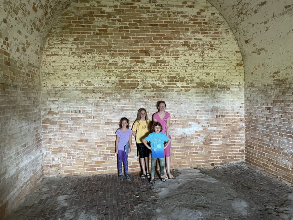 A photo of Ainsley, Dillon, Grayson, and Rayleigh in a large vaulted space in the fort made out of brick