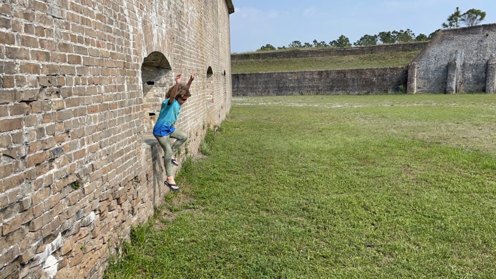 A photo of Grayson jumping out of a hole on the outside of a fort wall