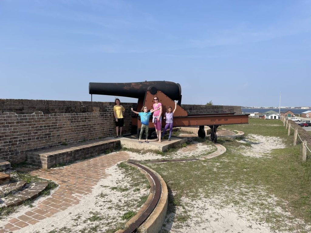 A photo of Dillon, Grayson, Rayleigh, and Ainsley in front of a large cannon on an exterior wall of the fort
