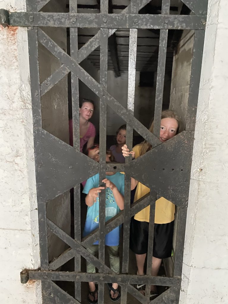 A photo of Rayleigh, Grayson, Ainsley, and Dillon behind a metal door in a jail cell in the fort