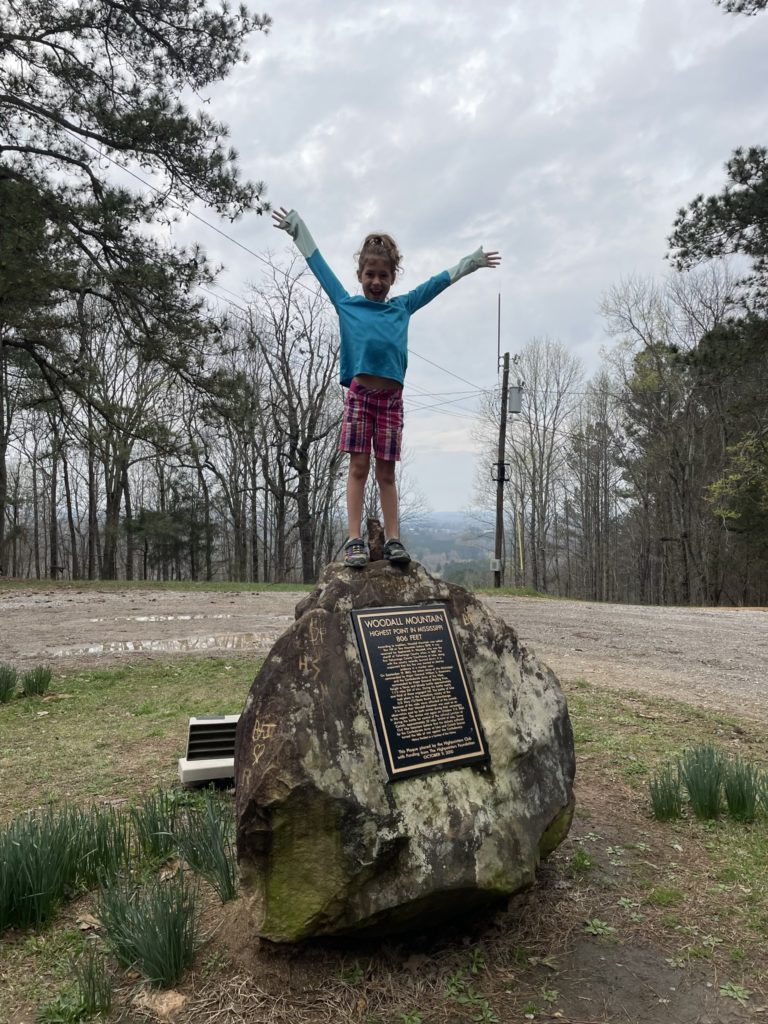 A photo of Ainsley standing on top of a large rock with her hands in the air