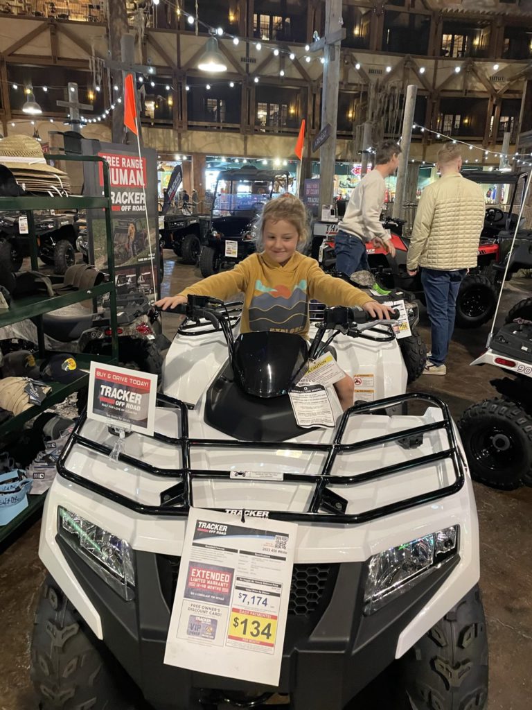 A photo of Grayson pretending to drive a white ATV with a price tag of $7,174