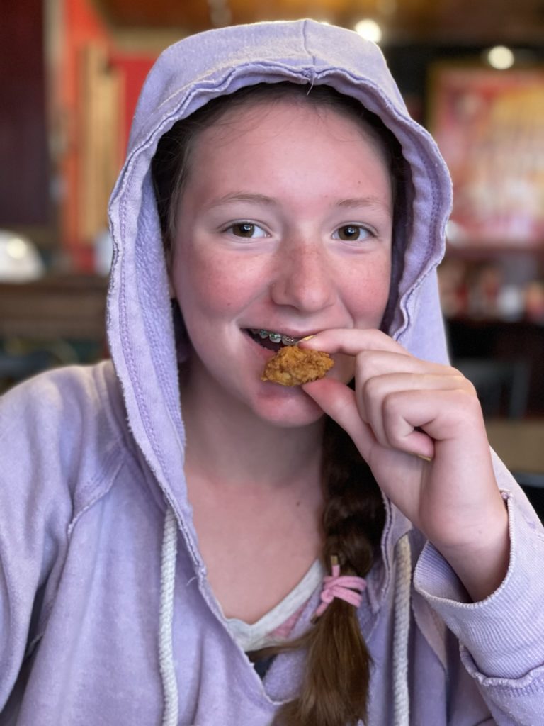A photo of Rayleigh in a hoodie with her hood up eating an alligator bite in a restaurant