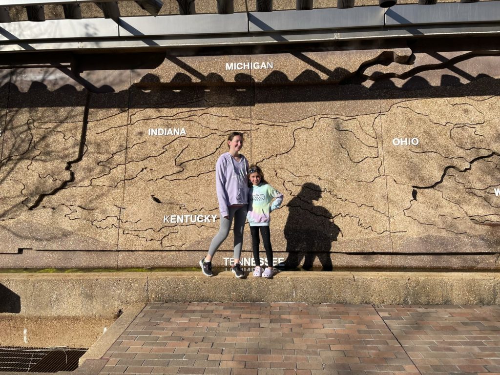 A photo of Rayleigh and Ainsley standing in front of a wall with the Mississippi River watershed on it, including areas of Michigan, Indiana, Kentucky, and Ohio