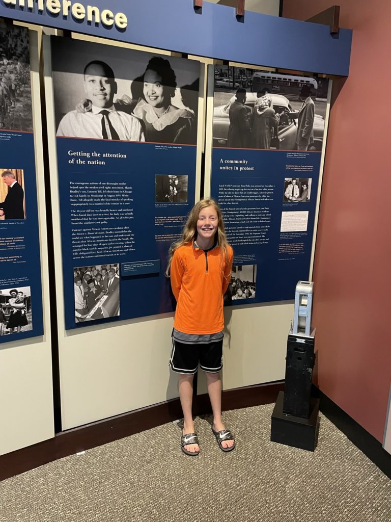 A photo of Dillon standing in front of a museum display about the Little Rock Nine that says "getting the attention of the nation"