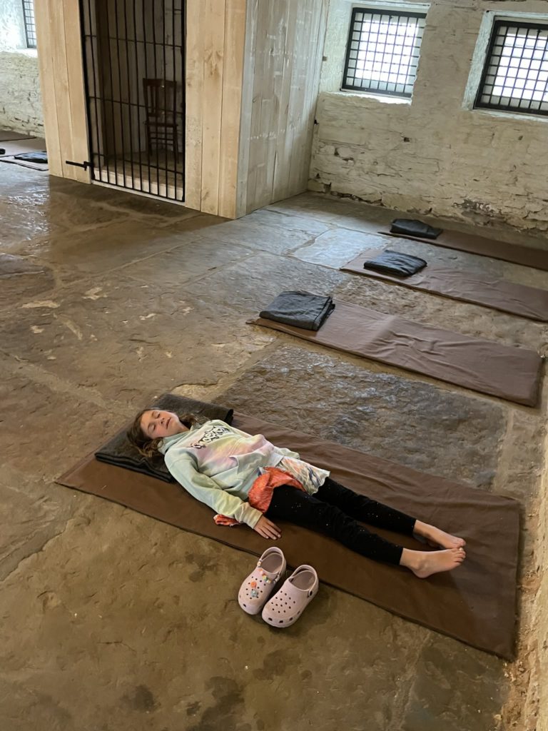 A photo of Ainsley laying on a spartan bedroll on the floor of the Fort Smith jail