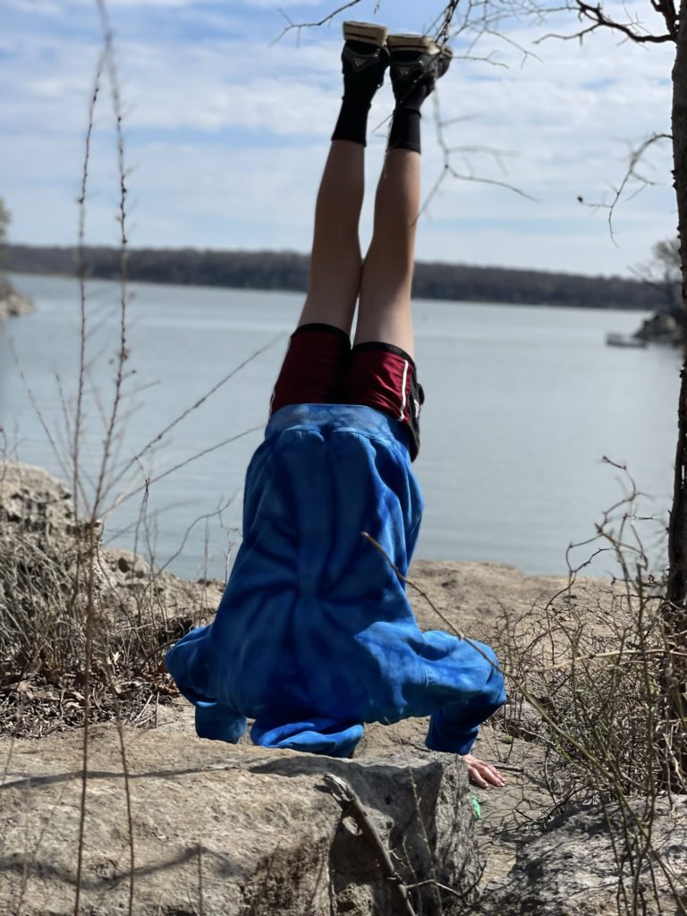 A photo of Dillon doing a headstand on a rock with a lake in the background