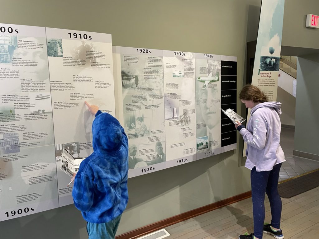 A photo of Dillon and Rayleigh working on their Junior Ranger books in front of a timeline of aviation history