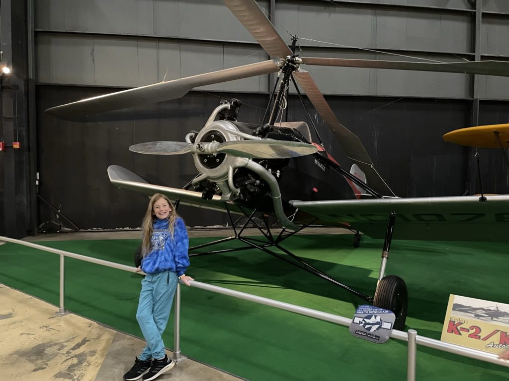 A photo of Dillon standing in front of an aircraft that looks like a combination of an airplane and a helicopter, with a front engine and prop, wings, and a four blade rotor on top