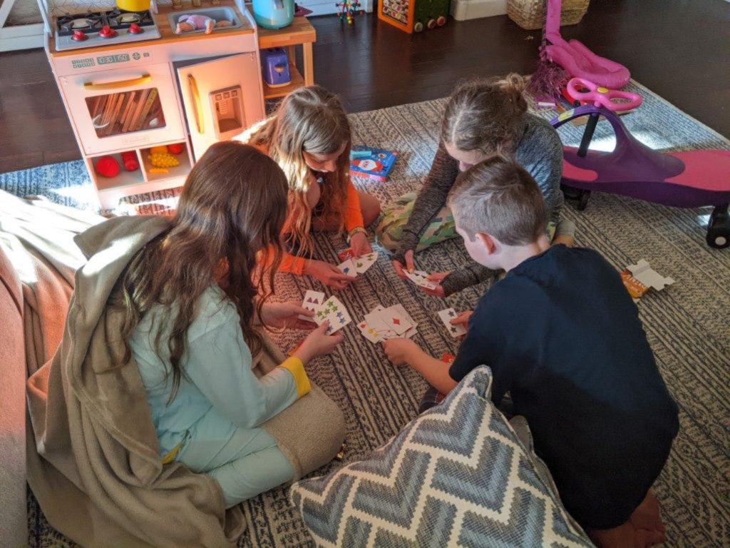 A photo of Myna, Dillon, Rayleigh, and Milo playing cards on the living room floor.